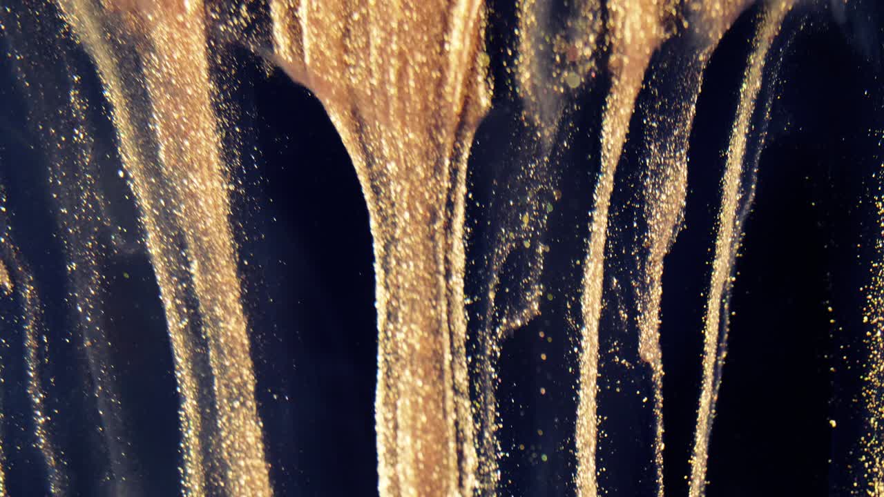 황금 잉크 입자는 검은 바탕에 다채로운 혼란으로 물에 흐른다.