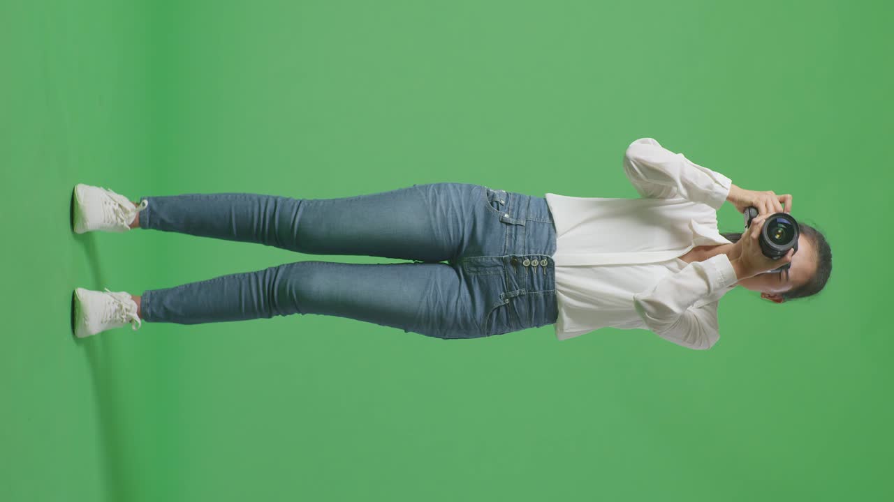 Full Body Of Tried Asian Photographer After Using A Camera Taking Some Pictures While Standing On Green Screen Background In The Studio