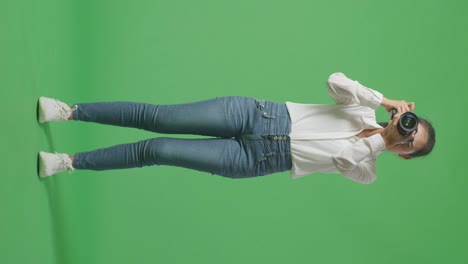 cuerpo lleno de fotógrafo asiático probado después de usar una cámara tomando algunas fotos mientras estaba de pie en el fondo de la pantalla verde en el estudio