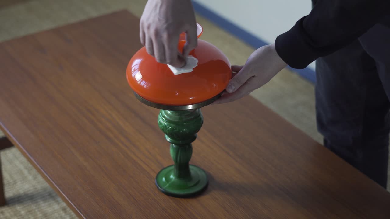 Hænder justerer en vintage bordlampe på et træbord og gør den klar til salg, vurdering, videresalg eller udstilling i en antikvitetsbutik