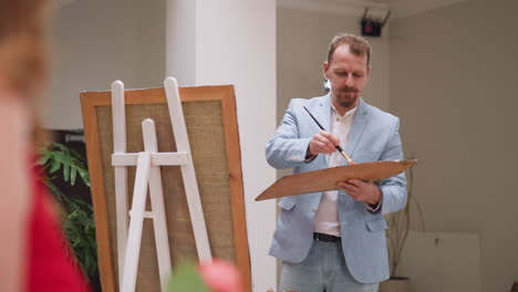 artist mixes colors with brush on palette. skilled painter starts painting young woman with choosing colors in well-lit studio. artwork by maestro