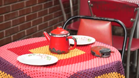red teapot on a colorful crocheted tablecloth at an outdoor cafe