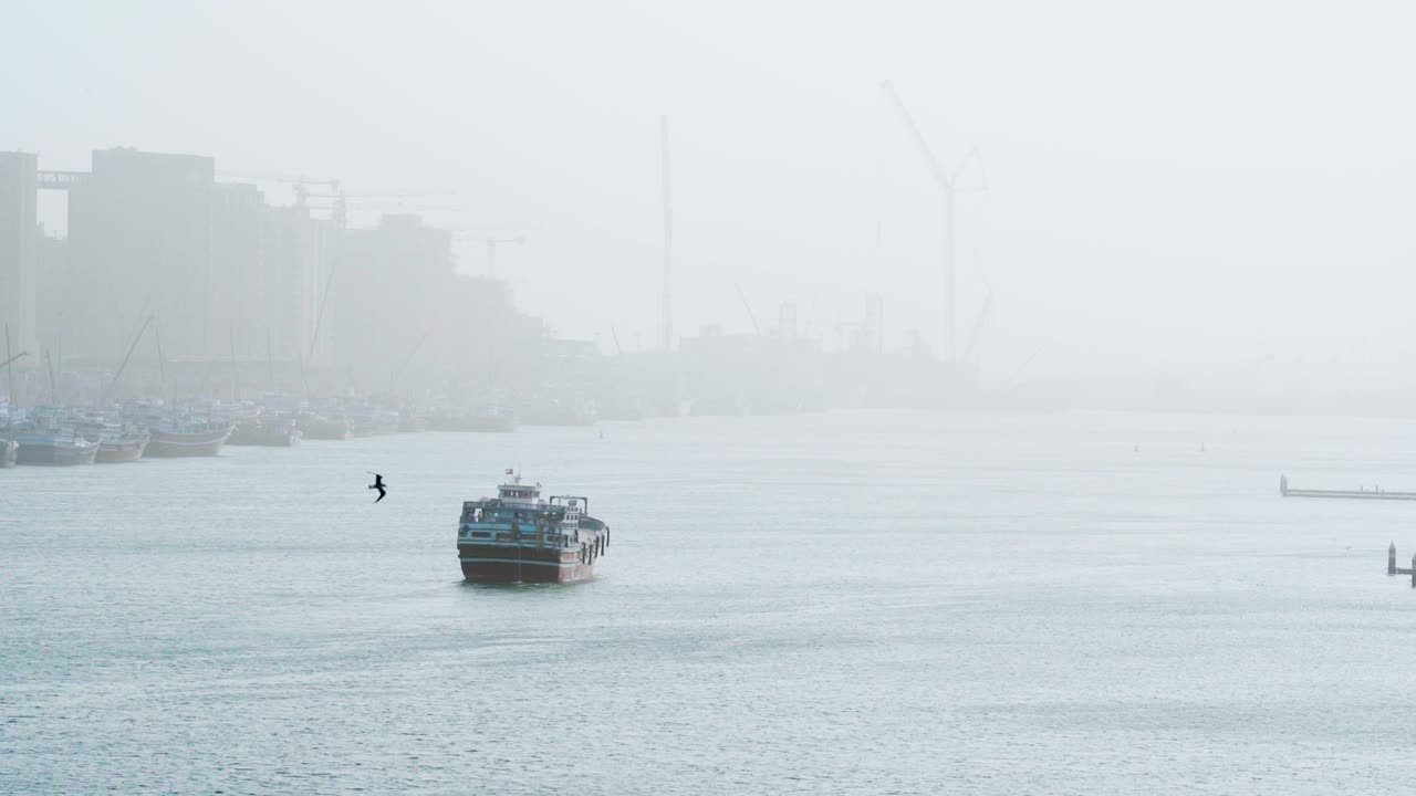 안개 낀 배경에 데이라 항구가 있는 두바이 크릭 한가운데 떠 있는 보트