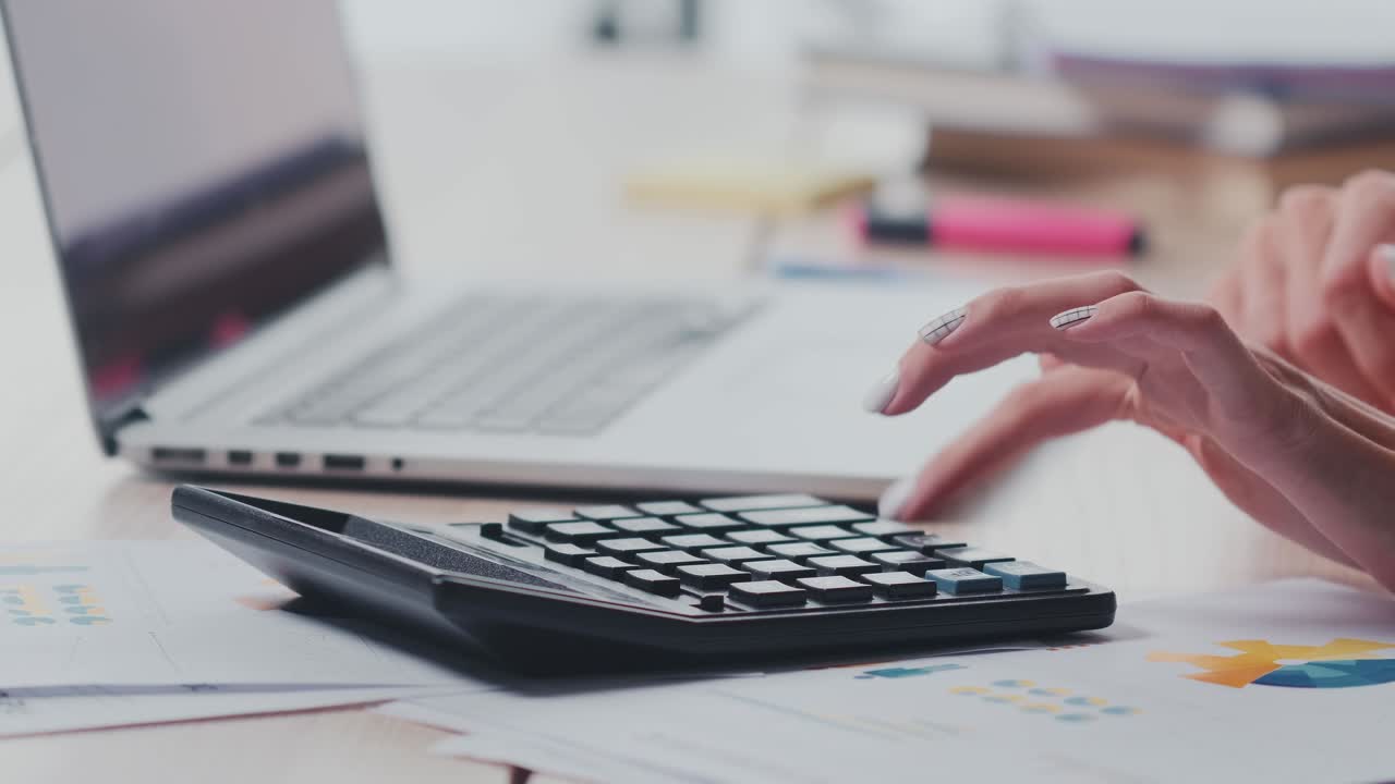 Close up of female hands pressing buttons of calculator and laptop