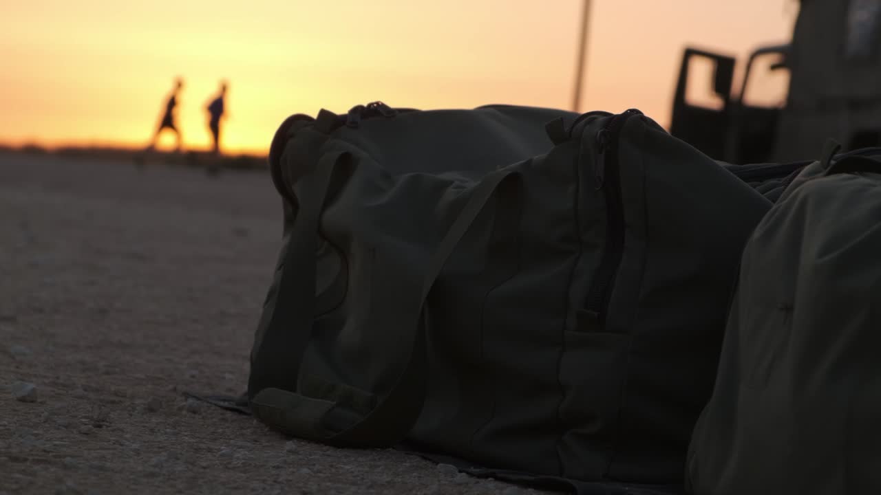 Military army bugs in the middle of the desert while in the background there is a military Vehicle and two soldiers jogging on the road during the amazing orange sunset next to a field