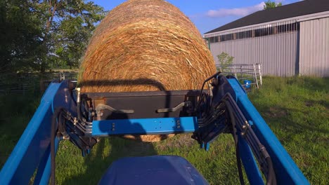 granjero que mueve grandes balas de heno utilizando un tractor azul en un granero rural