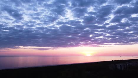 beautiful aerial vibrant high contrast pink purple sunset with blue clouds over baltic sea at liepaja, distant ships in the sea, wide angle ascending drone shot camera tilt down slow zoom in