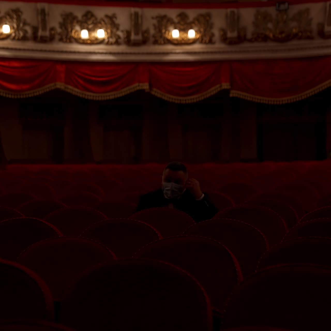 Man stands up from a red theater chair and throws medical mask away. Visitor in empty hall. Stop pandemic concept
