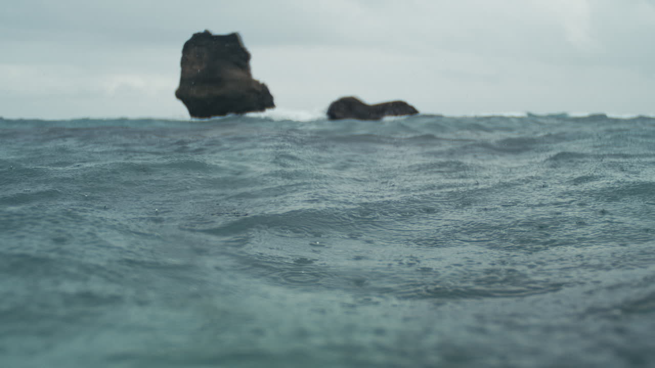 Calm ocean surface with island cliffs in the distance under soft sky