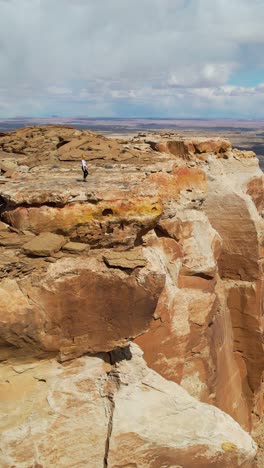 person walking on a dramatic desert cliff overlooking badlands