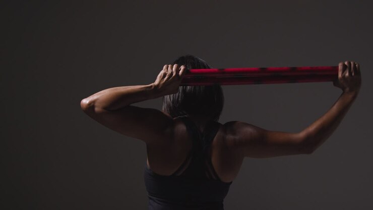 vista trasera de estudio de una mujer madura con ropa de gimnasia haciendo ejercicio con palos de artes marciales escrima 2
