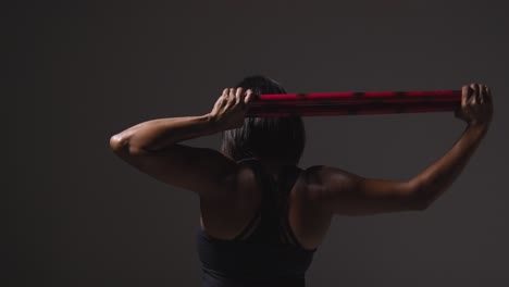 vista trasera de estudio de una mujer madura con ropa de gimnasia haciendo ejercicio con palos de artes marciales escrima 2