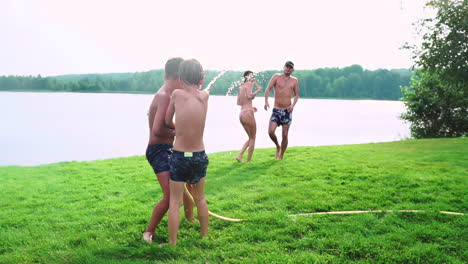 Sonniger-Sommertag-Auf-Dem-Rasen.-Familie-Mit-Zwei-Kindern-Hat-Spaß-Beim-Spielen-Mit-Wasser-Und-Beim-Lachen.-Fröhliche-Atmosphäre-Einer-Glücklichen-Familie