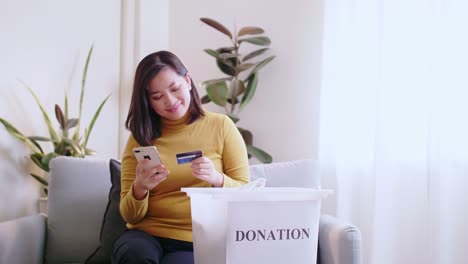 Woman-pressing-phone-using-a-credit-card-to-pay-online-to-reserve-donation-box-delivery