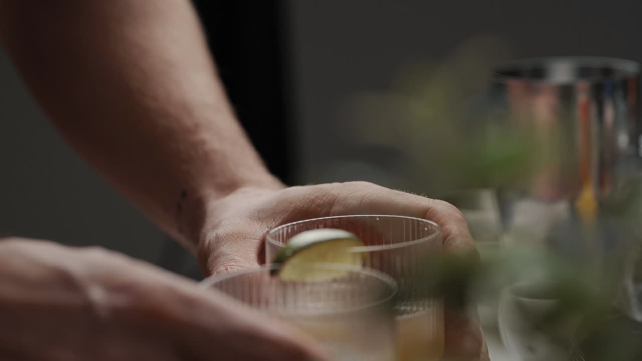 Young male grabbing two cocktails in modern drinking glasses in the kitchen at home decorated with a lime. Slow Motion