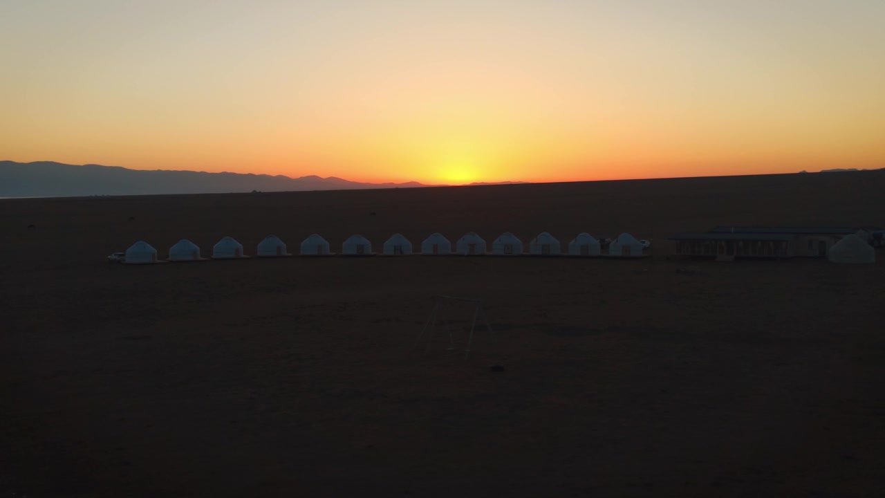 Ripresa panoramica aerea di un tradizionale accampamento di yurte nomadi allineate su un altopiano alpino al tramonto dorato vicino al lago Song-Kul, Kirghizistan