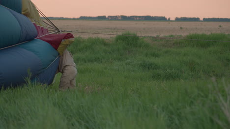 woman working on hot air balloon envelope in tall grass preparing envelope for inflation during sunset field preflight operation showcasing focus teamwork and vibrant fabric