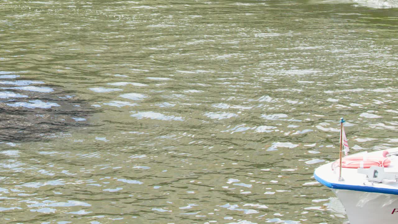 Tour boat moves past yellow warning sign on sunlit urban river, daylight, steady camera