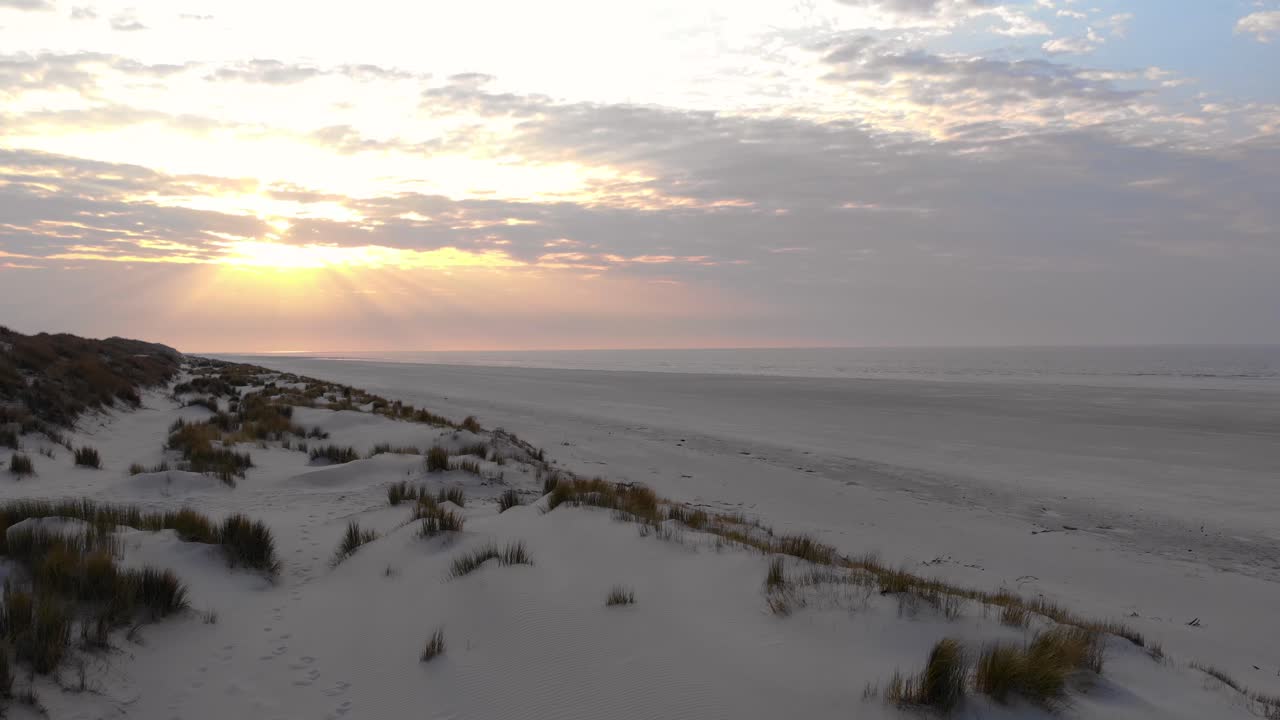 Aerial, rising, drone shot over dunes, at a beach, on Langeoog island, cloudy sunset, in North Germany