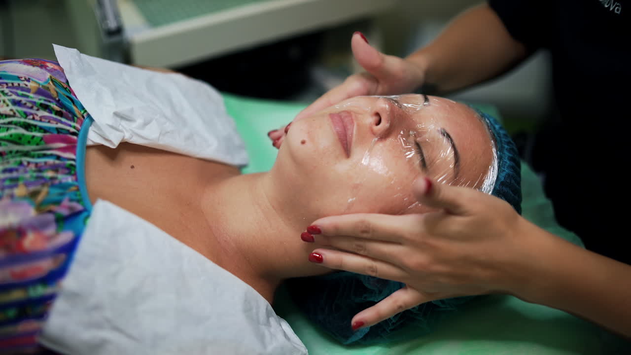 Beautician covering female client's face with cellophane. Cosmetologist preparing a woman for cosmetic skincare procedures. Close up.