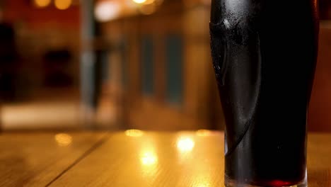 a detailed view of a dark stout glass resting on a wooden table with warm lighting.