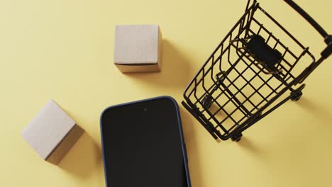 video of smartphone with blank screen, boxes, shopping trolley on yellow background