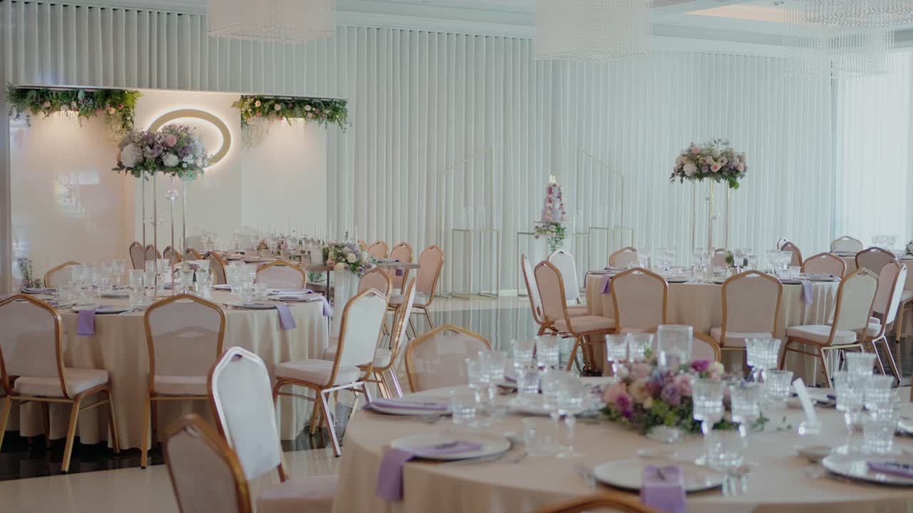Lavender accented wedding tables arranged with fine glassware, floral centerpieces, and gold chairs