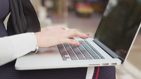 close up shot of woman sat outside typing-working on her laptop as people walk past