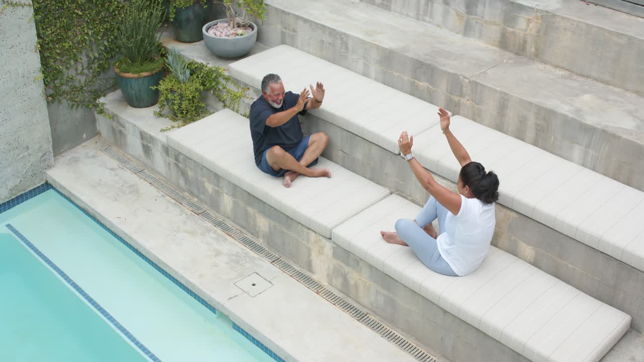 After stretch cue African American couple mirroring raising arms leaning reaching legs resting pool