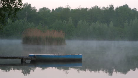 wooden rowboat lies steadily in the morning mist on a fogy forest lake