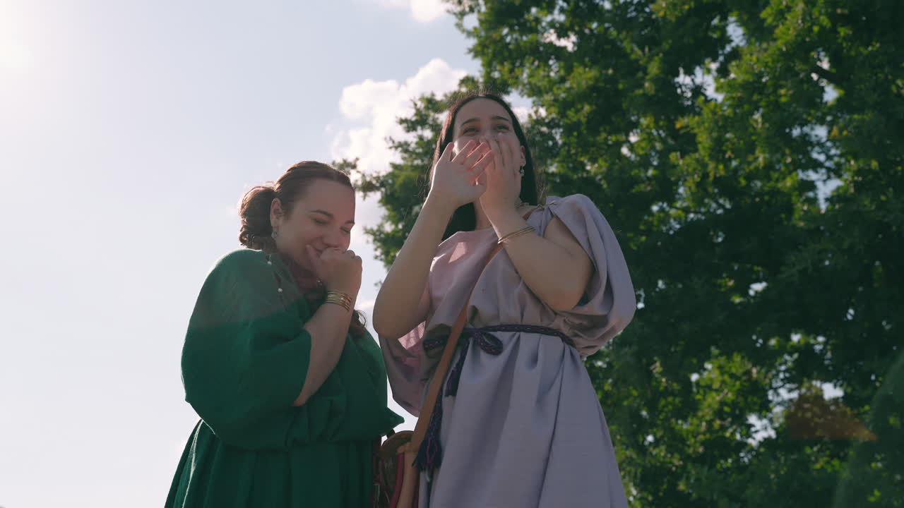 Two Women Laughing Outdoors in Historical Costumes