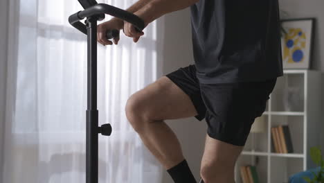 retired man is training alone at home spinning pedals of exercycle for good physical condition keeping body in fit details shot