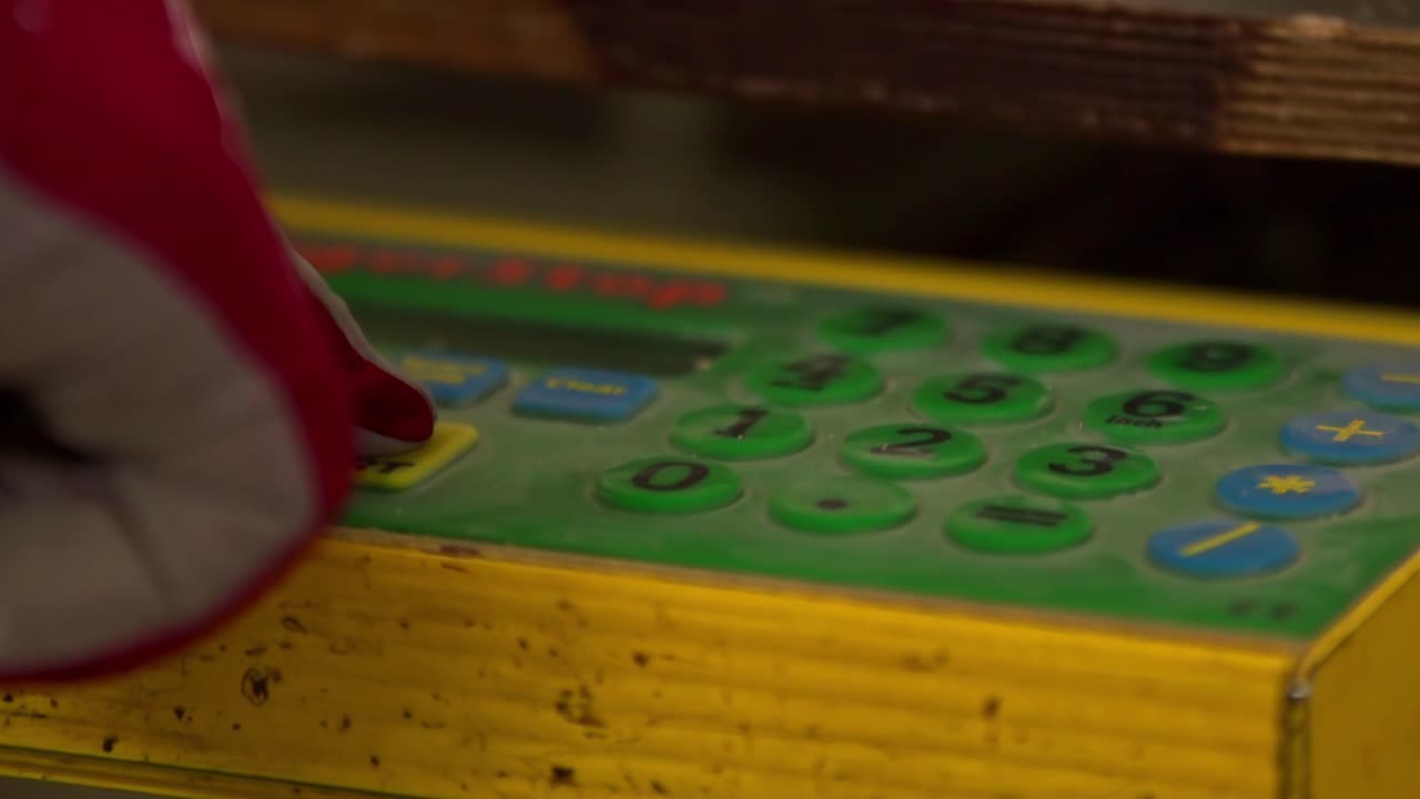 Gloved worker presses machine buttons and starts automated cycle in industrial setting