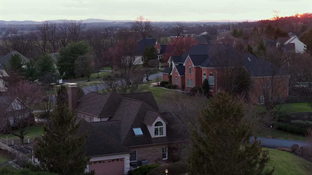 Aerial drone view of luxury suburban neighborhood at sunset in United States, with large mansion houses, landscaped properties and warm evening light over quiet residential area. Rise shot