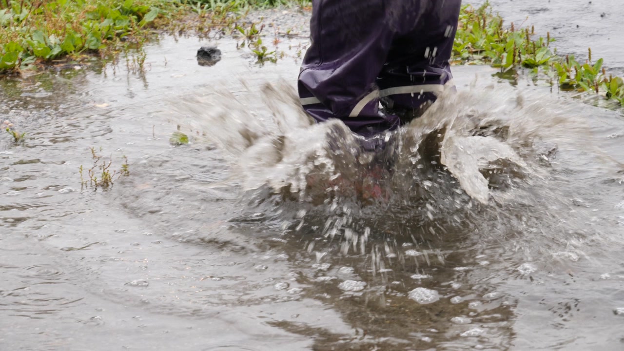 Adorable child playing and jumping in a rain puddle - slow motion