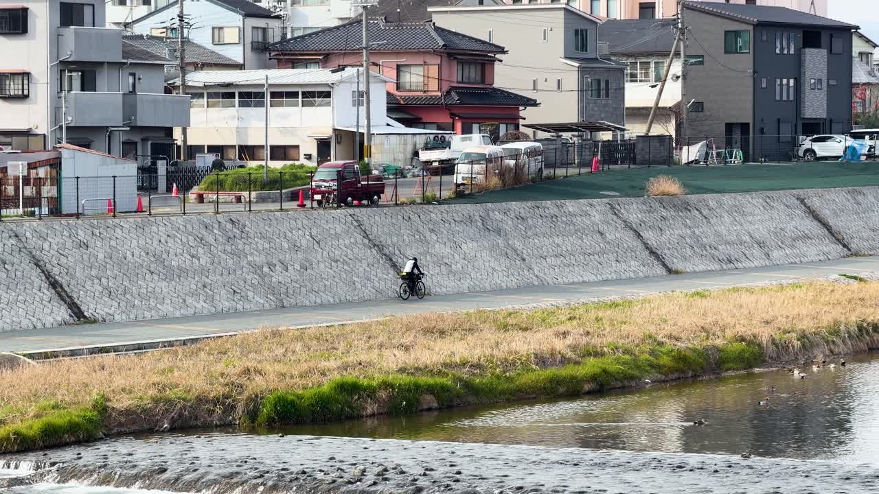 鴨川沿いの住宅街を自転車で走行するサイクリストを捉えたワイドショット。