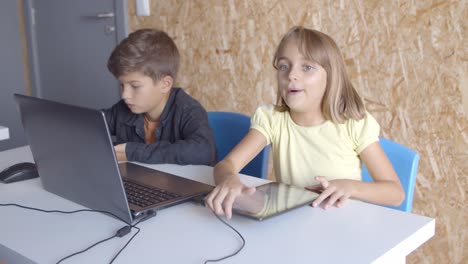 Focused-school-boy-and-girl-using-tablets-in-class