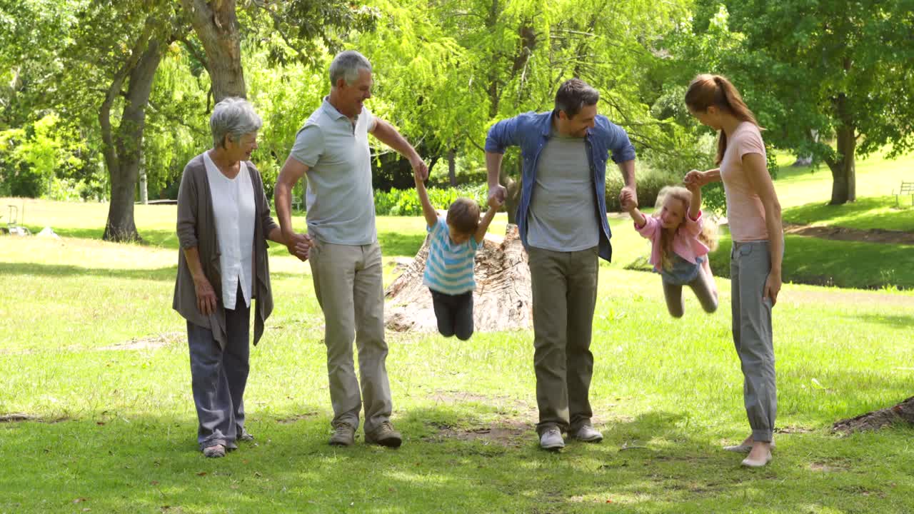 familia de varias generaciones sonriendo y tomados de la mano en un parque