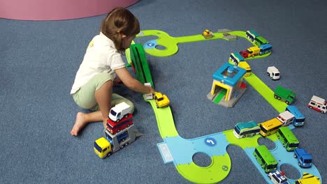 3-year-old-Toddler-Girl-Playing-With-Toy-Cars-Sitting-on-Floor,-Stacking-Autos-and-Drive-Them-On-Ramp-Road