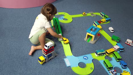 niña pequeña de 3 años jugando con coches de juguete sentada en el suelo, apilando autos y conduciéndolos por la rampa de la carretera