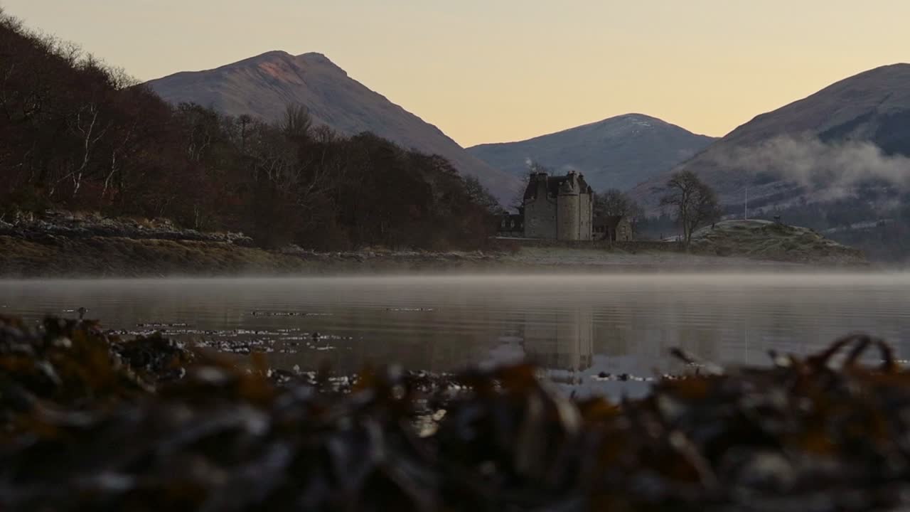 The Famous Dunderave Castle Situated On The Lakeshore In Loch Fyne, Argyll and Bute, Highlands of Scotland With Scenic Mountains In The Background - Wide Shot