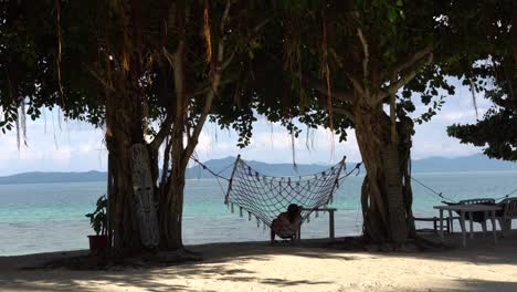 woman resting on a net hammock under the shady trees in dos palmas island resort in puerto princesa, palawan, philippines - medium shot