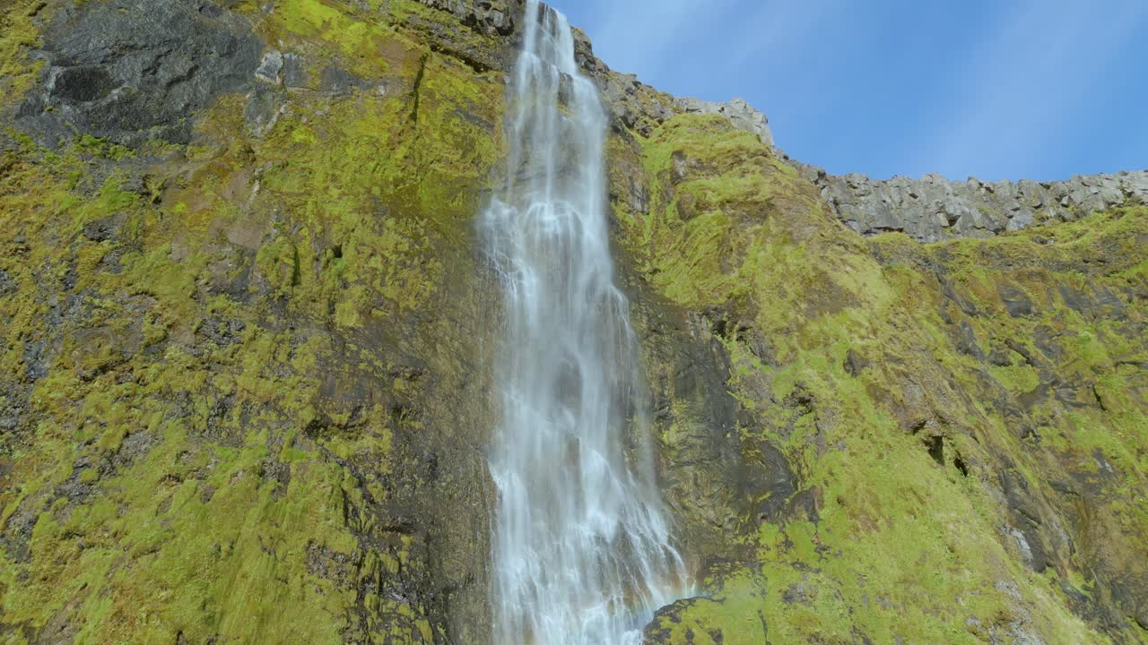 mirando una cascada que fluye sobre una roca de musgo verde en un día azul brillante