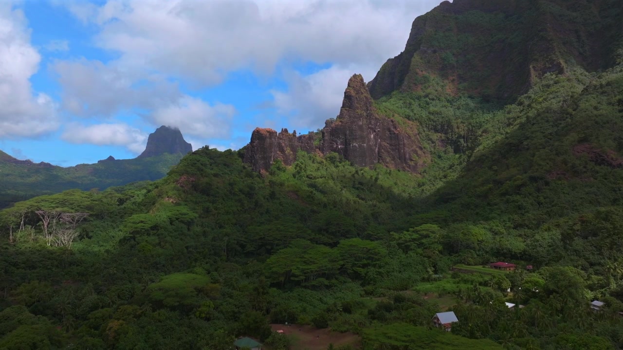 Cooks Opunohu Bay, strandhus, Mount Rotui, Mt Toheia, dramatiska vulkaniska höga taggiga toppar, oländig terräng, Moorea Franska Polynesien, flygdrönare, Belvedere utsiktsplats, solig morgon, blå himmel, moln, framåt.