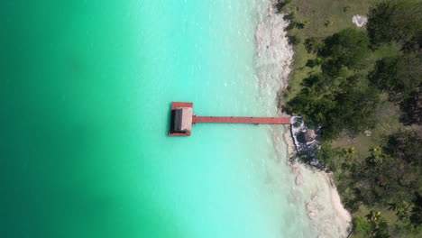 Dron-Cinemático-Descendente-Disparado-Hacia-Un-Muelle,-Muelle-Y-Cabaña-Cerca-De-Bacalar-México-Con-Aguas-Turquesas