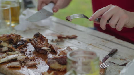 close up on hands of man cutting piece of slow roasted beef ribs on picnic table