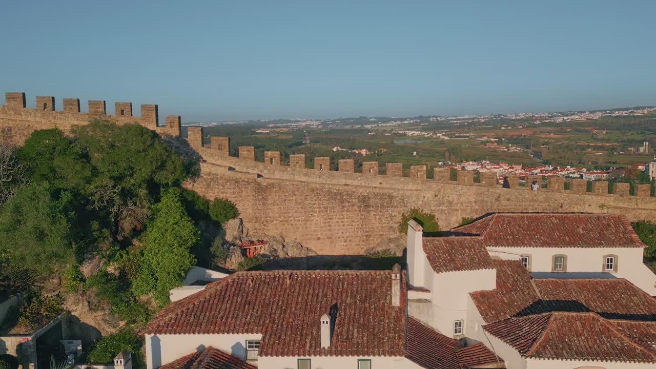 Stone castle walls surrounding historic town on  green hills drone view