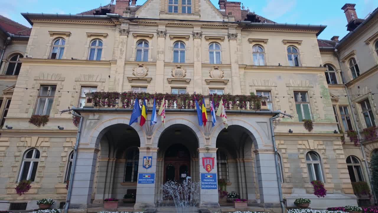 Tilt-up view of the stunning entrance and building of the Sighișoara city hall behind the fountain in Romania