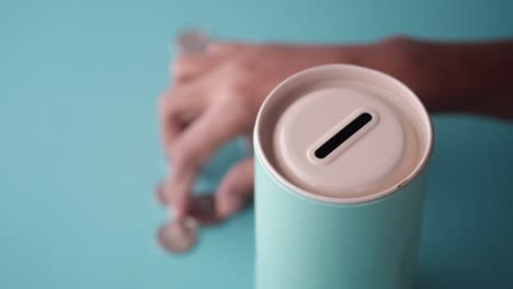 hand putting coins into a mint green cylindrical money box