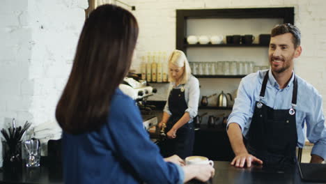 Rückseite-Der-Brünetten-Kundin,-Die-An-Der-Bar-Im-Café-Sitzt-Und-Der-Kellner-Ihr-Eine-Tasse-Kaffee-Gibt